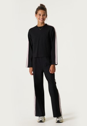 Camiseta negra de manga larga con rayas rosas en las mangas, combinada con pantalones anchos negros. Ambos hechos de una tela suave. Ropa deportiva casual.
