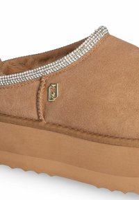 Scarpe slip-on in suede color talpa con fodera in finta pelliccia, arricchite da una fila di cristalli trasparenti lungo il colletto e una suola in gomma scolpita.