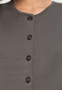 Γκρι πλεκτή ζακέτα με στρογγυλή λαιμόκοψη και έξι μαύρα κουμπιά κατά μήκος του μπροστινού μέρους, με ομαλή υφή και εφαρμοστή γραμμή.