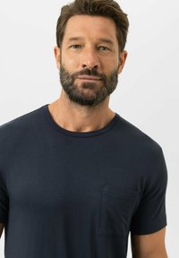 Granatowy bawełniany t-shirt z okrągłym dekoltem i krótkimi rękawami, z małą kieszonką na piersi po lewej stronie. Gładka faktura.