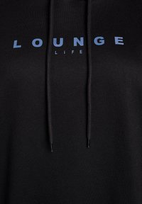 Felpa nera con un logo frontale che recita "LOUNGE" in azzurro chiaro. Presenta dei lacci e un tessuto morbido e texturizzato.