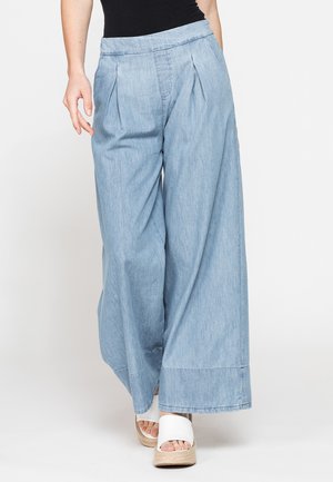Pantaloni a gamba larga azzurri chiaro con pieghe, indossati con sandali platform bianchi aperti in punta e un top nero, mostrati dalla vita ai piedi.