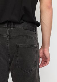 Zwarte denim jeans met een rechte pijp, voorzien van een achterzak en een leren logo label. De stof lijkt enigszins vervaagd en textuur te hebben.