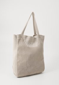 Beige vævet tote taske med struktureret stof, dobbelte håndtag og en let forlængelse foroven. Har et subtilt logo foran.