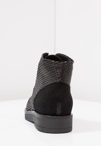 Botín negro hasta el tobillo con un exterior texturizado de imitación de piel de serpiente y material de gamuza suave. Suela plana y lisa con punta redondeada.