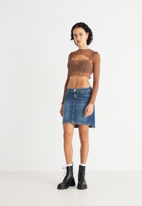 Brown long-sleeve crop top with cut-out details paired with a blue denim mini skirt. Black lace-up boots and white ankle socks.
