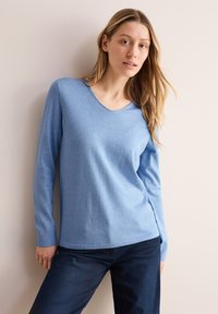 Ljusblå, långärmad V-ringad tröja med en slät textur, i kombination med mörka jeans. Designen är enkel med en avslappnad passform.