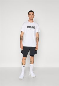 Hvit bomull T-skjorte med teksten "SEIER STARTER MED TRAING" , svarte shorts, hvite sokker og hvite joggesko.