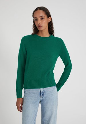 Pullover verde lavorato a maglia con scollatura rotonda, polsini e orlo a costine, e una texture morbida. Abbinato a jeans in denim azzurro chiaro.