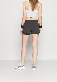 Pantalones cortos deportivos negros con un diseño en capas, combinados con una camiseta corta blanca y zapatillas blancas con detalles en negro y dorado.