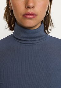 Maglione a collo alto ribbed blu scuro con un'estetica morbida, abbinato a orecchini a cerchio in argento. Vista ravvicinata.
