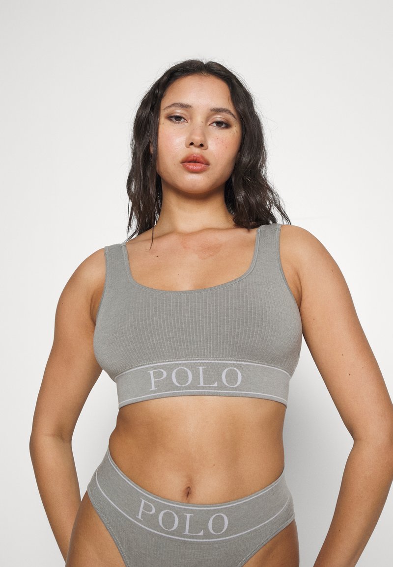 Bralette cinza com textura em nervuras e cueca coordenada com uma faixa de logotipo. O material é macio e elástico, com alças largas e um design minimalista.