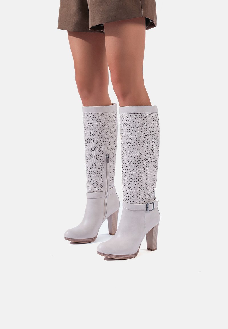 Stivali bianchi in pelle al ginocchio con design perforato, tacchi robusti, zip laterale e dettaglio della fibbia. Finitura morbida e forma strutturata.