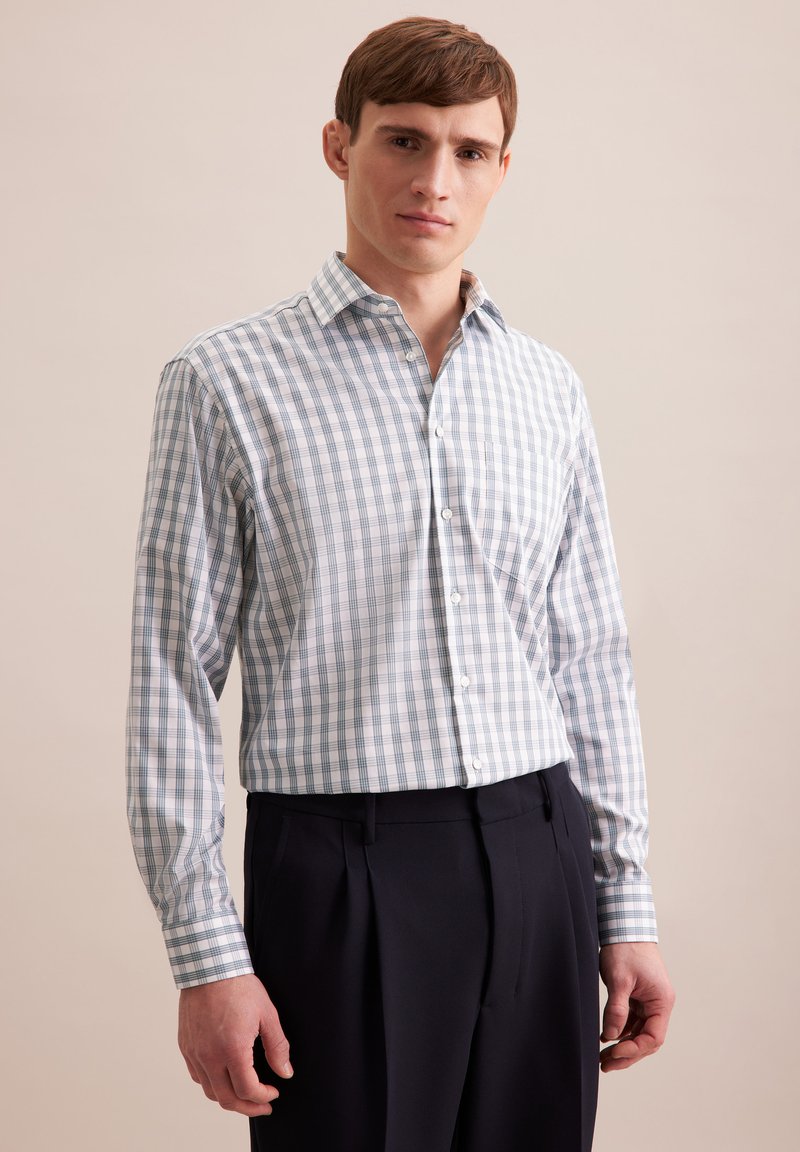 Camicia a quadri blu e bianca con maniche lunghe, design con colletto e bottoni bianchi, indossata con pantaloni scuri.