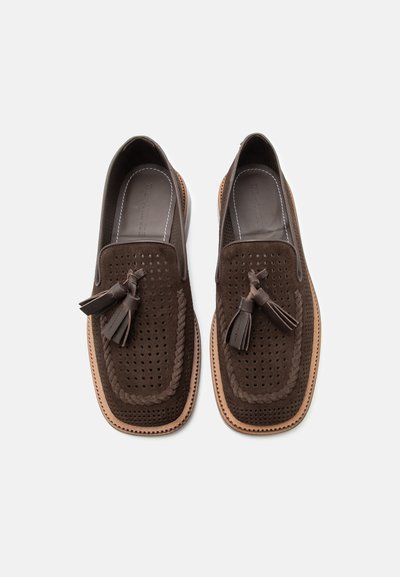 Mocassins en daim marron avec dessus perforé, bordure tressée et pompons en cuir sur une semelle marron clair, vus de dessus.