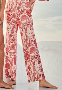 Pantalons à motifs rouges et blancs avec des designs floraux et de coquillages, en tissu léger, dotés de jambes larges et d'une coupe décontractée.