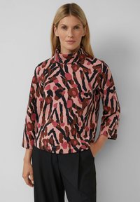 Langärmliges, pinkes Oberteil mit einem gemusterten Design, das dunkelbraune und schwarze Akzente aufweist. Der Kragen ist hoch und der Stoff scheint weich zu sein.
