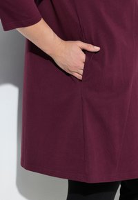 Bordeaux jurk met korte mouwen, voorzien van een zijzak, een gladde textuur en een rechte snit die net boven de knie valt.