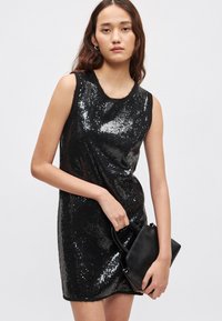 Μαύρο αμάνικο φόρεμα καλυμμένο με παγιέτες, εφαρμοστό σχέδιο, λεία υφή, συνδυασμένο με μικρή μαύρη τσάντα.