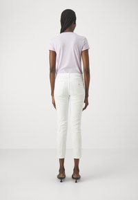 Fialové tričko spárováno s bílými kalhotami na míru, které zvýrazňují přiléhavý střih. Oblečení zahrnuje štíhlou siluetu a minimalistické akcenty.