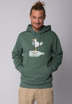 Groene hoodie met een vooraanstaande graphic van een meeuw die op een fles staat, met een papieren bootje erin. Zachte stof en capuchon met trekkoord.
