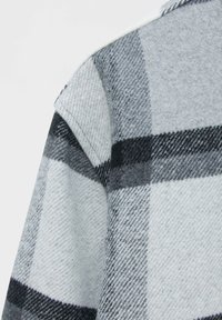Gray and black plaid flannel fabric, featuring a soft texture and sharp contrast between large squares and thin lines, with a standard collar.