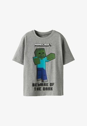 Grå kortærmet t-shirt med grafik af en Minecraft-figur. Teksten lyder "VÆR OPMÆRKSOM PÅ MØRKET" i fed sort skrift. Blødt stof.