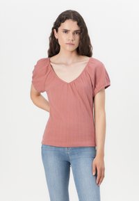 Top ribbed roz prăfuit cu decolteu în V larg și mâneci bufante. Textură netedă, silueta ajustată, asociat cu blugi albaștri deschiși.