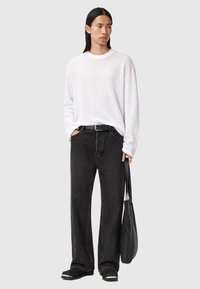 Hvid tekstureret sweater, løse sorte jeans, sort bælte og sort taske. Langt hår og minimalistisk fodtøj fremhæver det afslappede look.