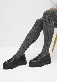 Grå mönstrade strumpbyxor med en texturerad design, i kombination med svarta läderloafers med en tofs och tjock plattformsula.