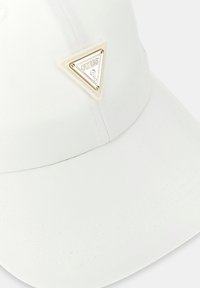 Casquette de baseball blanche en tissu avec une surface texturée. Présente un patch logo triangulaire de couleur dorée à l'avant.