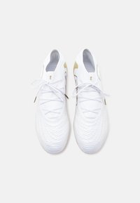 Ζευγάρι λευκά αθλητικά παπούτσια με υφαντή υφή, λευκά κορδόνια και χρυσές λεπτομέρειες, απεικονιζόμενα από πάνω σε απλό φόντο.