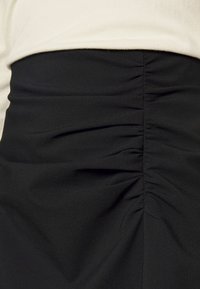 Černá shromážděná látka v oblasti pasu oděvu, spárovaná s svetrem v světlém béžovém odstínu.