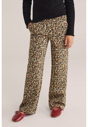 Pantaloni a gamba larga con stampa leopardata in beige, marrone e nero, realizzati in tessuto morbido. Abbinati a scarpe basse rosse e a un top a maniche lunghe nero.