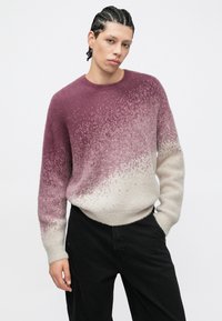 Pletený sveter s prechodovým vzorom z tmavofialovej do krémovej farby, so soft textúrou a okrúhlym výstrihom. Nosí sa s čiernymi nohavicami.
