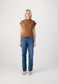 Bruin gestructureerd T-shirt met korte mouwen en een gegolfde zoom, gecombineerd met rechte blauwe jeans en lichtgekleurde sandalen. Eenvoudig en casual ontwerp.