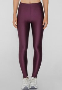 Leggings bordeaux a vita alta realizzati in un tessuto elastico lucido, design aderente, texture liscia, abbinati a scarpe da ginnastica bianche.