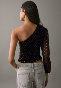 Top nero in tessuto arricciato con una manica a sbuffo e tessuto trasparente decorato; presenta orlo arricciato e accenti metallici su tutta la superficie.