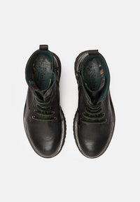 Botas de cuero negro hasta el tobillo con cordones verdes y forro interior, con punta redonda y suela texturizada, vistas desde arriba.
