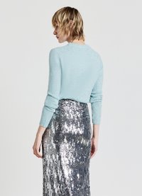 Hellblauer, strukturierter Strickpullover mit langen Ärmeln, kombiniert mit einem silbernen Paillettenrock, der eine figurbetonte Silhouette und einen schimmernden Effekt aufweist.
