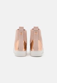 Sneakers alte color rosa pallido con tessuto in rete, dettagli metallici color oro rosa, suola bianca e una linguetta sul retro. Presentano un dettaglio con bottone del logo.