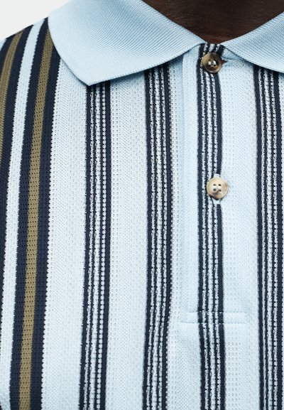 Φωτεινό γαλάζιο πλεκτό πόλο μπλουζάκι με κάθετες λωρίδες σε ναυτικό μπλε, μαύρο και ελιά, με δύο κουμπιά μπροστά.