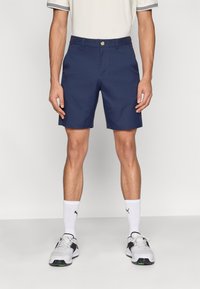 Σκούρα μπλε βερμούδα από ύφασμα μείγματος βαμβακιού, με εφαρμοστή σχεδίαση, θηλιές για ζώνη και κούμπωμα με κουμπί στο μπροστινό μέρος.