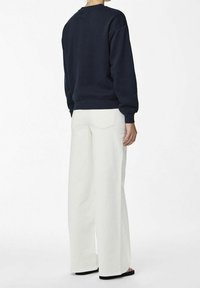 Mörkblå sweatshirt med rund halsringning, i kombination med högmidjade, vida vita byxor. Slät textur och avslappnad passform.