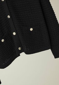 Zwarte gebreide cardigan van textiel, met gouden knopen, twee voorzakken en een geribbelde zoom en manchetten.