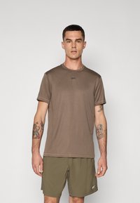 T-shirt marron à manches courtes avec un col rond et un logo discret sur la poitrine, associé à un short vert olive. Texture lisse.