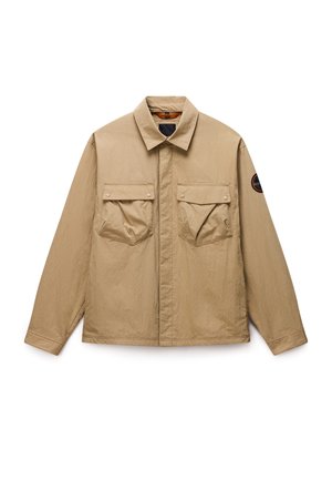 Beige Freizeitjacke mit langen Ärmeln und spitzem Kragen, zwei vorderen aufgesetzten Taschen mit Knopfklappe und rundem schwarzem Aufnäher am rechten Ärmel.