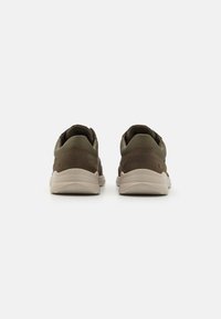 Brown sneakers with a mix of textured suede and fabric upper, featuring a cushioned sole in cream color. Reinforced heel and low-profile design.