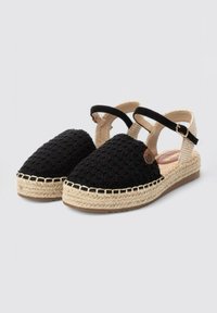 Sandalias espadrilles tejidas en negro con tira al tobillo, detalles de yute y parte superior texturizada. Presentan una puntera redonda y una suela plana.