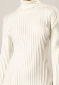 Ribbad vit polotröja i mjukt stickat tyg, med lång ärm och en kroppsnära passform. Strukturerat mönster över hela.